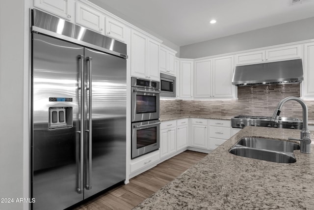 kitchen featuring light stone countertops, backsplash, sink, built in appliances, and white cabinets