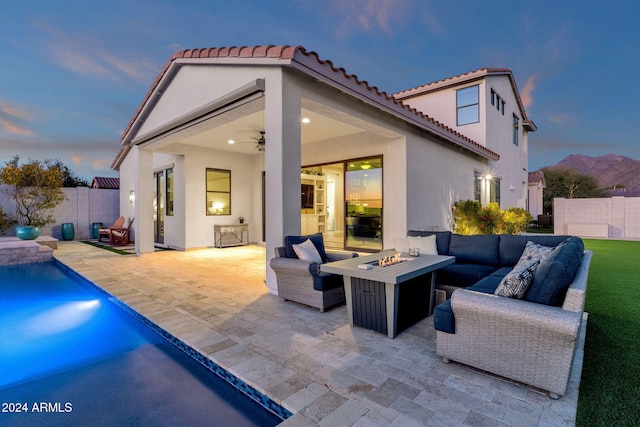 back house at dusk featuring a fenced in pool, a patio area, ceiling fan, and an outdoor living space with a fire pit