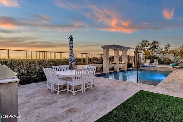 pool at dusk with a patio area, pool water feature, and an outdoor kitchen