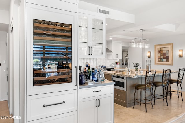 bar with hanging light fixtures, tasteful backsplash, wall oven, light stone counters, and white cabinets