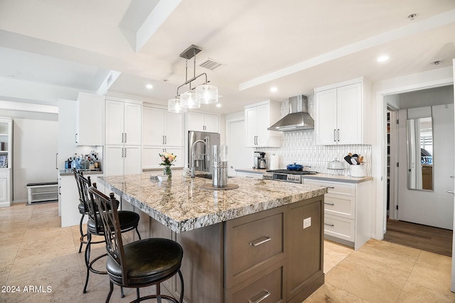 kitchen featuring light stone countertops, wall chimney range hood, pendant lighting, white cabinets, and an island with sink