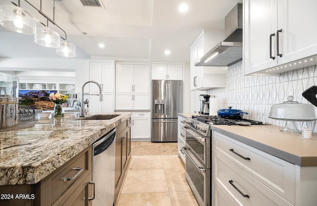 kitchen featuring sink, stainless steel appliances, wall chimney range hood, decorative light fixtures, and white cabinets