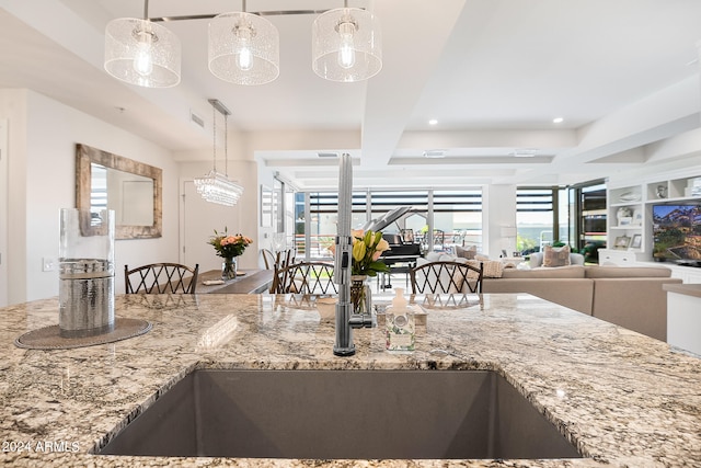 kitchen with light stone countertops, a wealth of natural light, hanging light fixtures, and sink