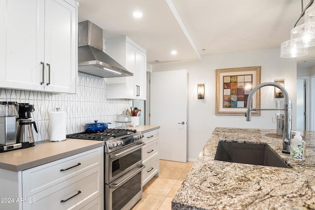 kitchen with white cabinets, sink, range with two ovens, and wall chimney range hood