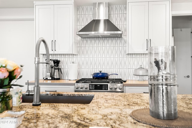 kitchen featuring light stone countertops, backsplash, white cabinetry, and wall chimney exhaust hood