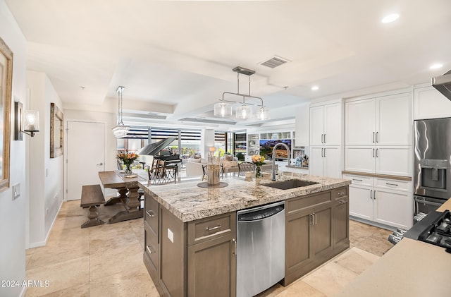 kitchen with white cabinetry, sink, stainless steel appliances, pendant lighting, and a center island with sink