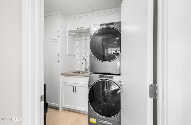 clothes washing area featuring cabinets, light tile patterned flooring, stacked washer / dryer, and sink