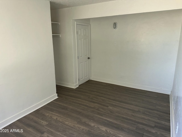 empty room featuring dark wood-type flooring, baseboards, and a textured ceiling