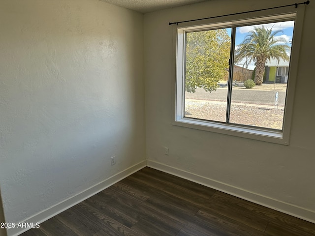 empty room featuring baseboards, dark wood-style flooring, and a textured ceiling