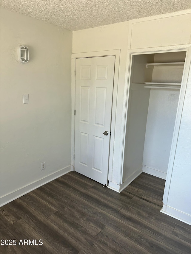 unfurnished bedroom with dark wood finished floors, baseboards, a closet, and a textured ceiling