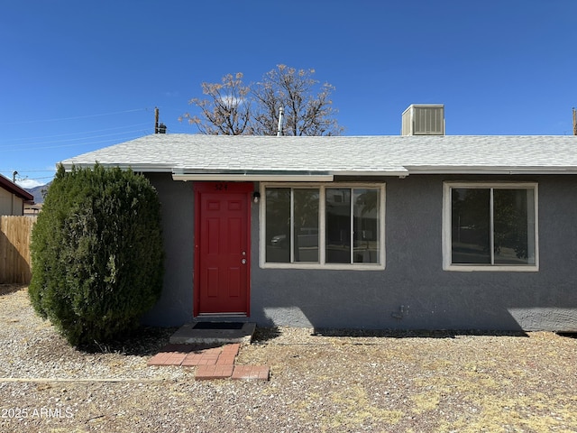 view of front of home with stucco siding, roof with shingles, and fence