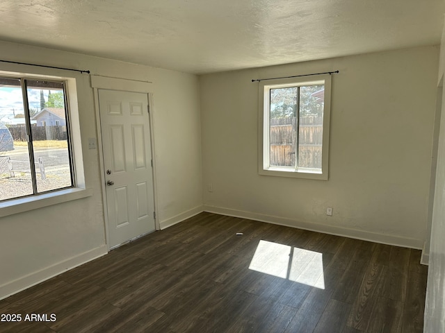 empty room with a textured ceiling, baseboards, and dark wood-style flooring