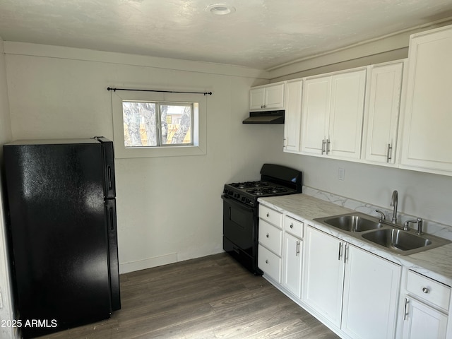 kitchen featuring black appliances, a sink, under cabinet range hood, wood finished floors, and white cabinetry