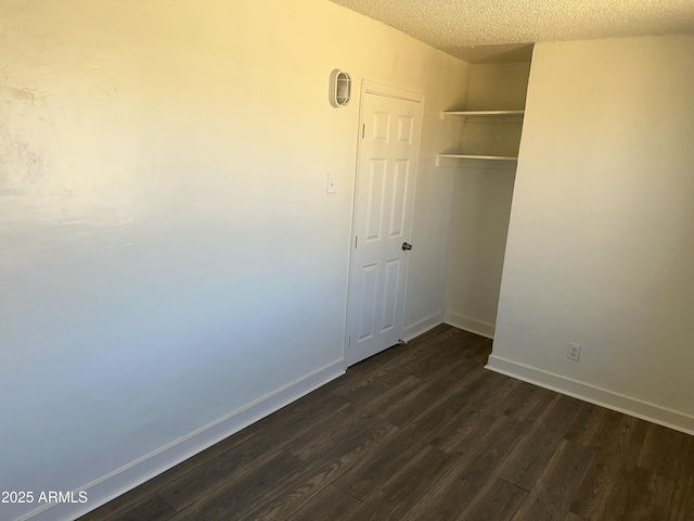 unfurnished bedroom with a closet, baseboards, a textured ceiling, and dark wood-style flooring