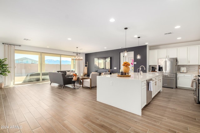 kitchen with sink, pendant lighting, light hardwood / wood-style floors, a center island with sink, and appliances with stainless steel finishes