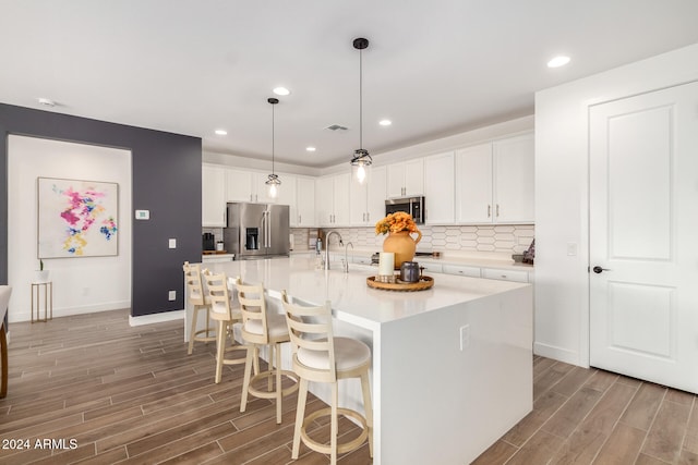 kitchen featuring stainless steel appliances, sink, white cabinets, hardwood / wood-style floors, and an island with sink