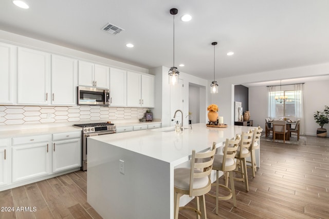 kitchen featuring white cabinetry, a center island with sink, stainless steel appliances, and light wood-type flooring