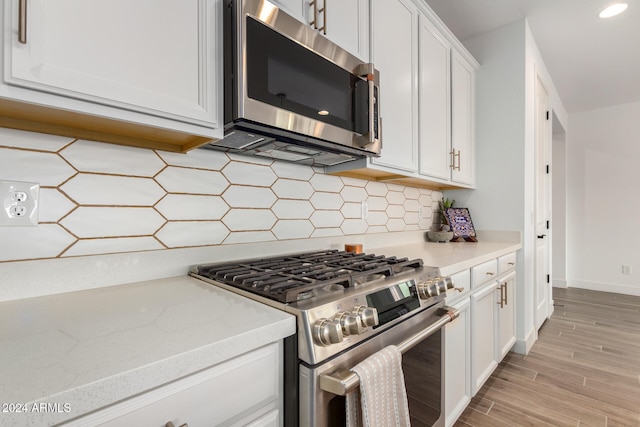 kitchen with light stone countertops, tasteful backsplash, stainless steel appliances, light hardwood / wood-style flooring, and white cabinetry