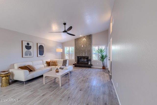 living room with ceiling fan, a large fireplace, lofted ceiling, and light wood-type flooring