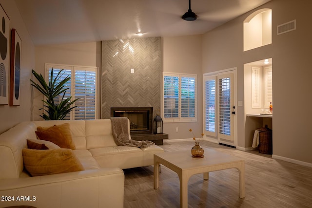 living room with wood-type flooring, a large fireplace, tile walls, and lofted ceiling