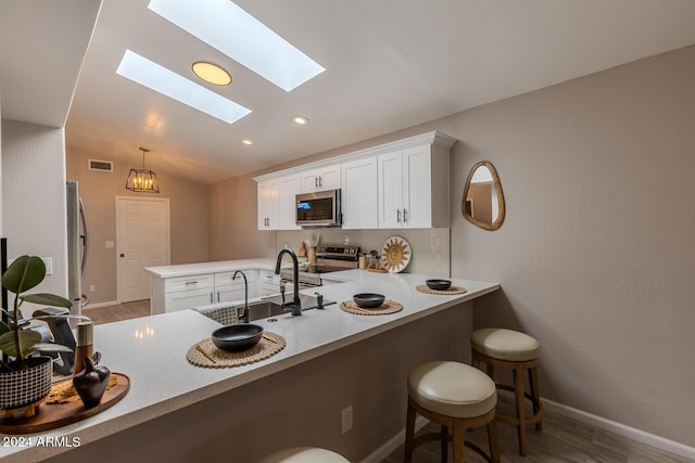 kitchen with stainless steel appliances, kitchen peninsula, lofted ceiling with skylight, a breakfast bar area, and white cabinets