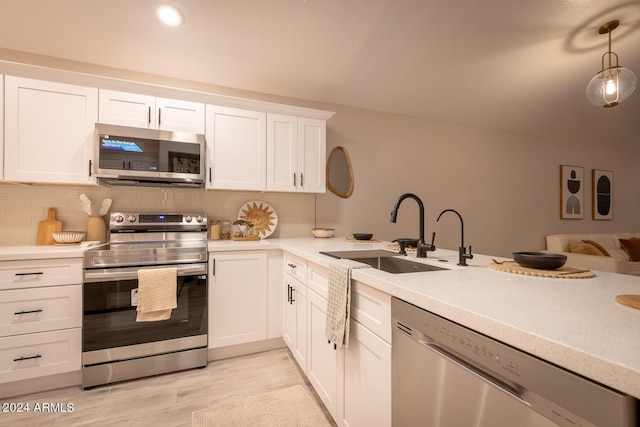 kitchen with sink, stainless steel appliances, tasteful backsplash, pendant lighting, and white cabinets