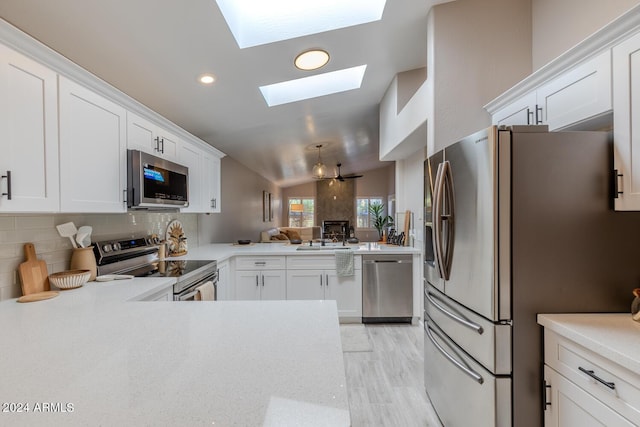 kitchen featuring white cabinetry, backsplash, kitchen peninsula, lofted ceiling with skylight, and appliances with stainless steel finishes