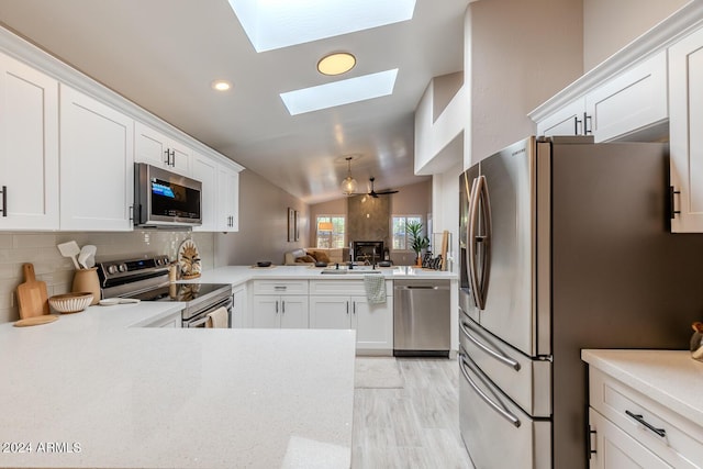 kitchen with backsplash, kitchen peninsula, lofted ceiling with skylight, white cabinets, and appliances with stainless steel finishes