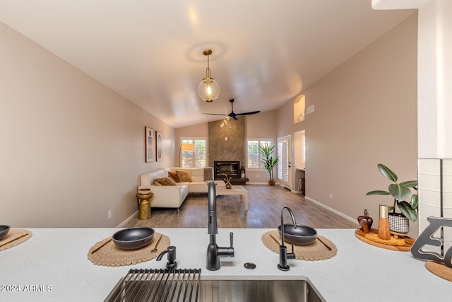 kitchen featuring dark wood-type flooring, sink, vaulted ceiling, ceiling fan, and a fireplace