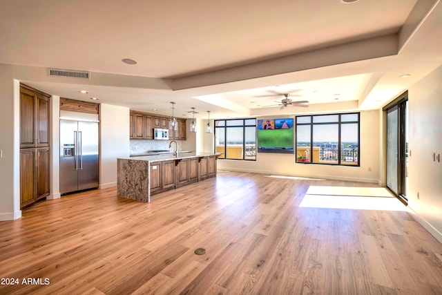 kitchen with decorative light fixtures, a kitchen island with sink, stainless steel appliances, and a raised ceiling