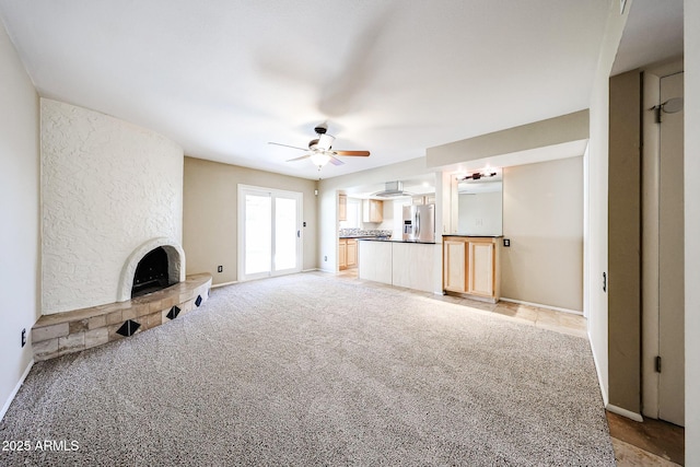 unfurnished living room with light colored carpet, a fireplace, baseboards, and a ceiling fan