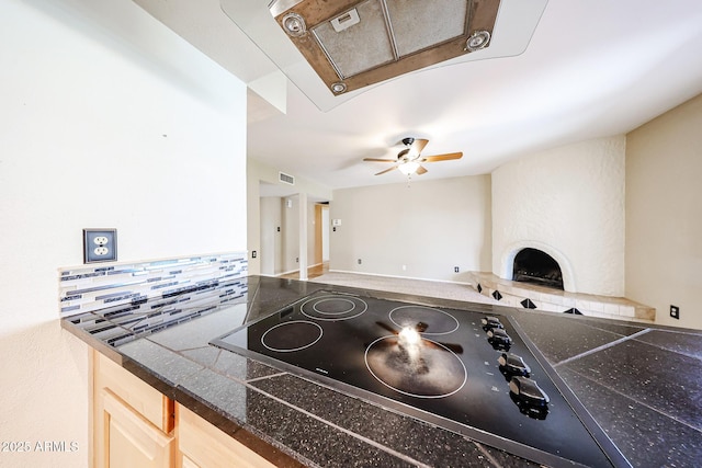 kitchen featuring visible vents, light brown cabinets, backsplash, a fireplace, and black electric stovetop