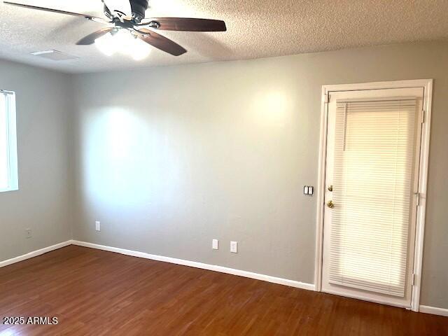 empty room with a textured ceiling, ceiling fan, and dark hardwood / wood-style flooring