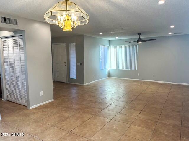 tiled empty room featuring ceiling fan with notable chandelier and a textured ceiling