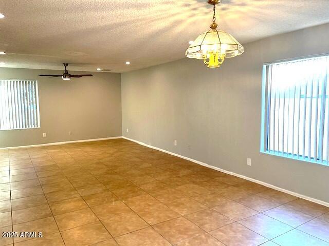 spare room featuring ceiling fan with notable chandelier, tile patterned flooring, and a wealth of natural light