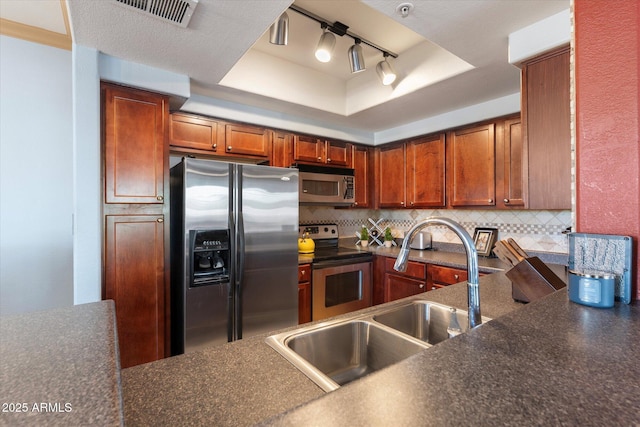 kitchen featuring a tray ceiling, a sink, stainless steel appliances, and dark countertops