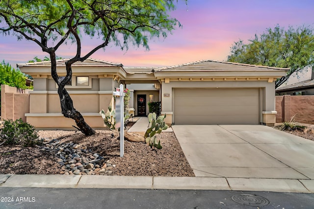 prairie-style home featuring concrete driveway, a tile roof, an attached garage, fence, and stucco siding