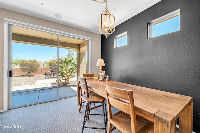 carpeted dining space featuring a chandelier, plenty of natural light, and a textured wall