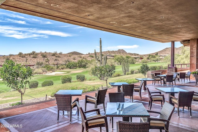 view of patio with outdoor dining space, view of golf course, and a mountain view