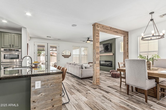 3109 N Black Rock Rd, Buckeye, AZ 85396 - kitchen featuring a sink, light wood finished floors, dark stone countertops, a ceiling fan, and a fireplace