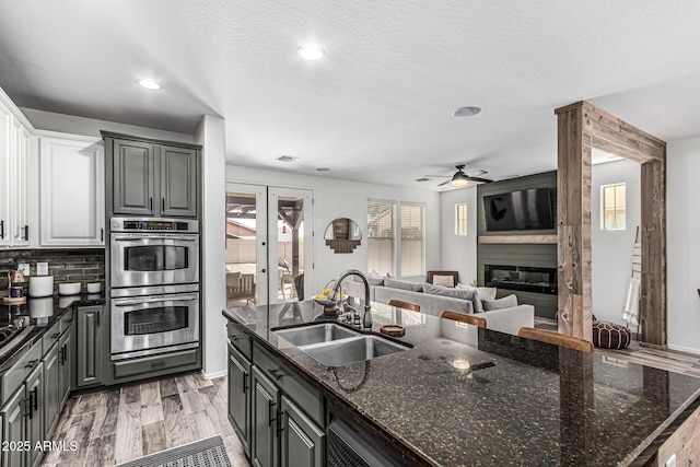 3109 N Black Rock Rd, Buckeye, AZ 85396 - kitchen featuring a sink, stainless steel double oven, a ceiling fan, a fireplace, and open floor plan
