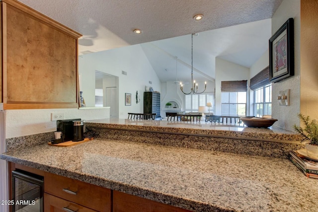 10015 E Mountain View Rd Unit 2012, Scottsdale, AZ 85258 - kitchen featuring brown cabinetry, an inviting chandelier, lofted ceiling, beverage cooler, and a textured ceiling