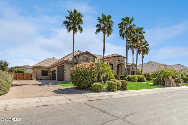 view of front of property with a garage, stone siding, fence, decorative driveway, and stucco siding