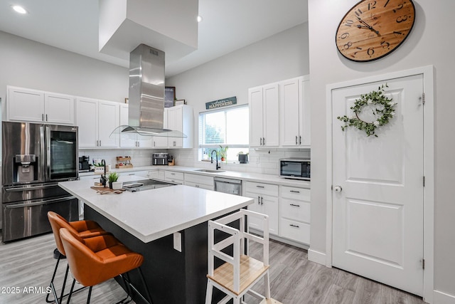 kitchen featuring island exhaust hood, a breakfast bar area, decorative backsplash, appliances with stainless steel finishes, and a sink