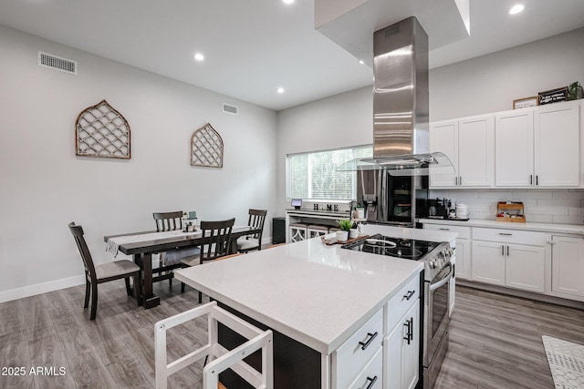 kitchen with a center island, light wood finished floors, stainless steel appliances, visible vents, and island range hood