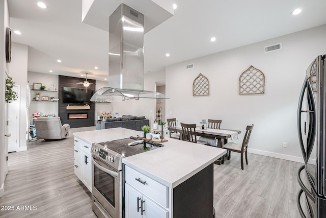 kitchen with a fireplace, visible vents, appliances with stainless steel finishes, white cabinets, and island range hood