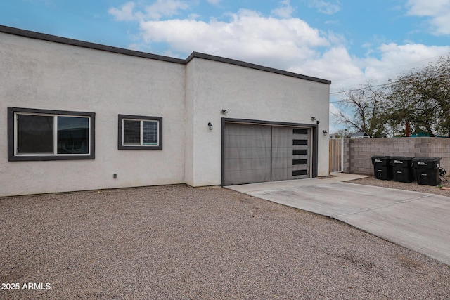 view of side of property featuring concrete driveway, an attached garage, fence, and stucco siding