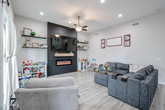 living room featuring ceiling fan, a fireplace, visible vents, and wood finished floors