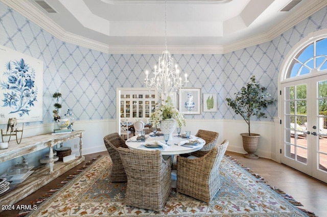 dining area featuring a tray ceiling, an inviting chandelier, hardwood / wood-style floors, crown molding, and french doors