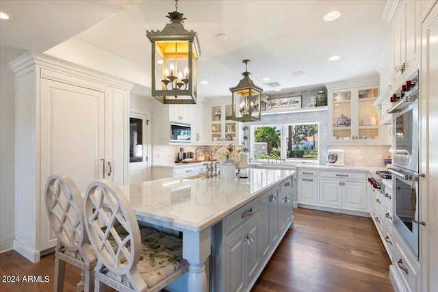 kitchen featuring pendant lighting, a center island, white cabinets, dark hardwood / wood-style flooring, and light stone countertops